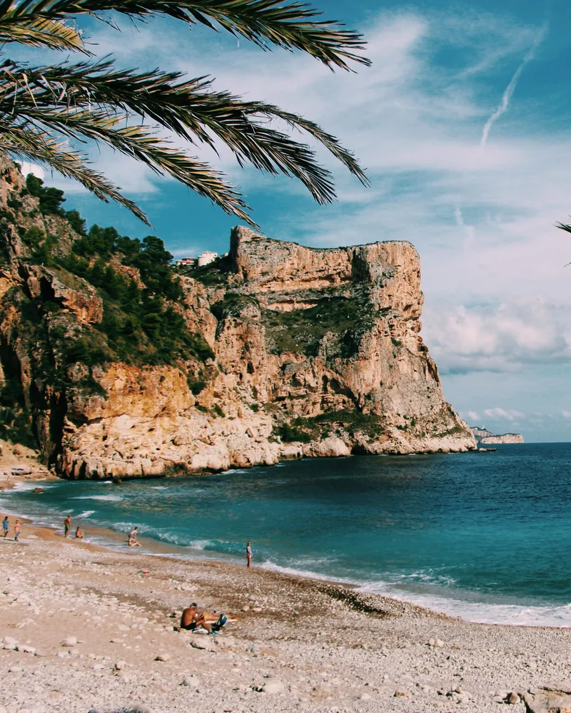 Cala de aguas turquesa con acantilado rocoso y palmeras en la Costa Blanca