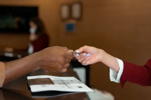 Recepcionista entregando una tarjeta a un huésped sobre el mostrador, junto al pasaporte y la documentación del registro