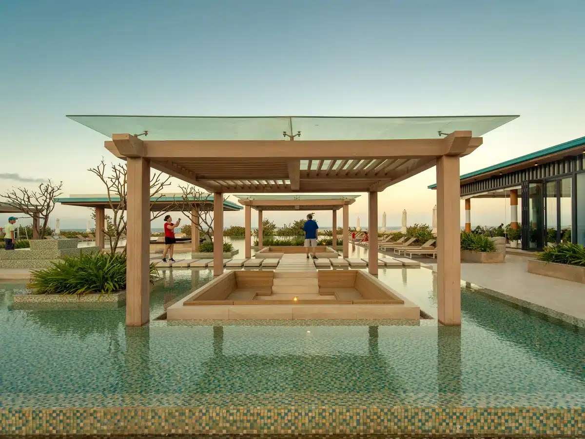 Piscina de un resort junto al mar con pérgolas de madera al atardecer