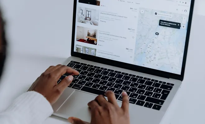 Persona buscando alojamiento en un portátil con un listado de habitaciones y un mapa de precios