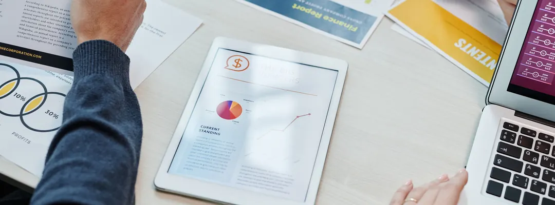 Manos revisando informes financieros con gráficas y datos junto a una tablet