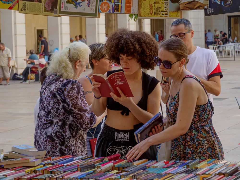 Varias personas ojeando libros en un puesto de un mercadillo de libros al aire libre