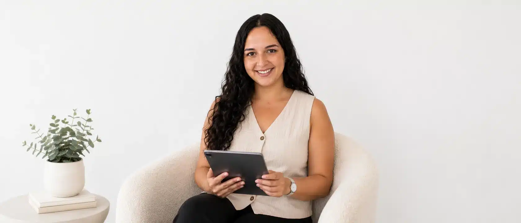 Oana Camaras trabajando con una tablet sentada en un sillón junto a una planta