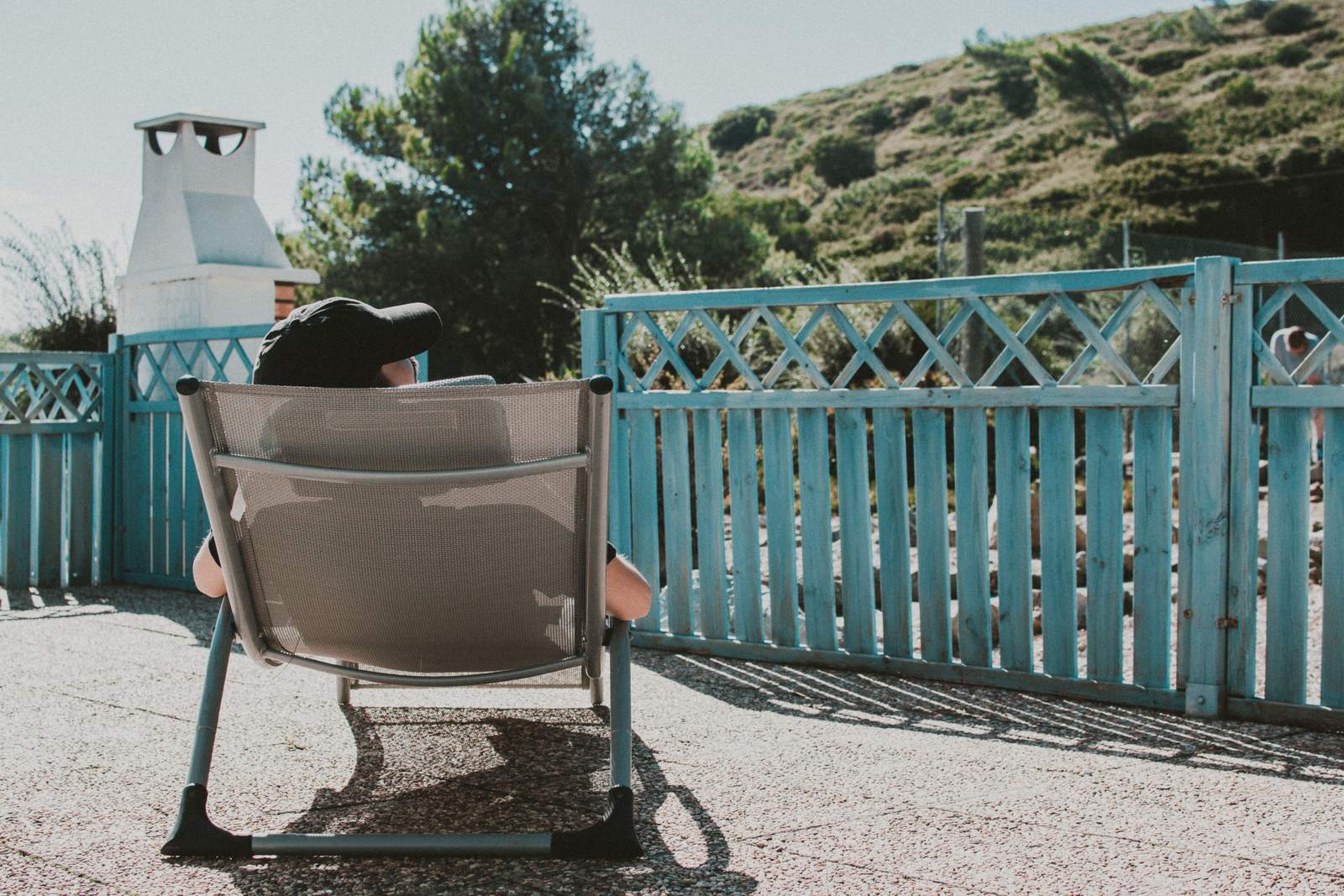 Persona sentada en una silla en la terraza de un alojamiento con vegetación mediterránea al fondo